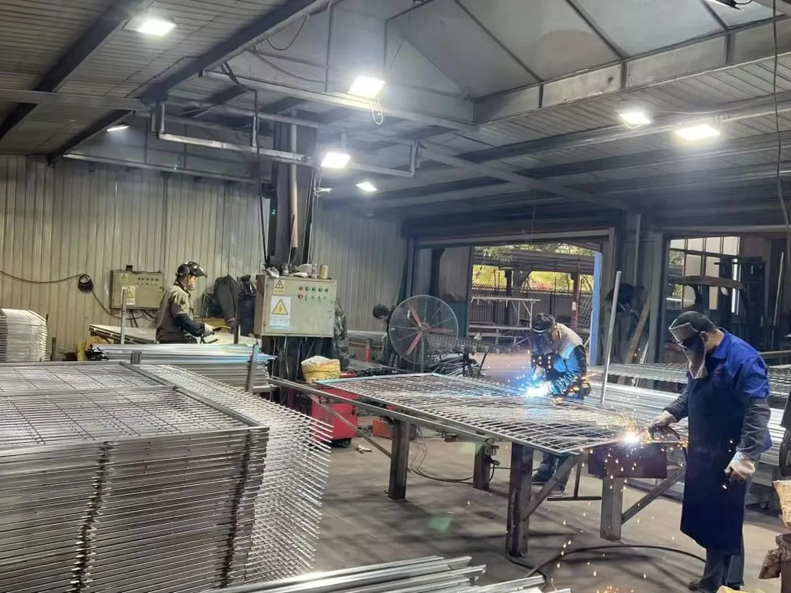 Workers welding steel fence panels in a production work area